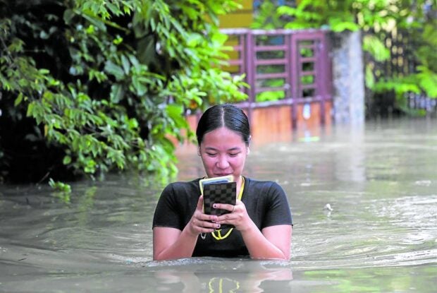 A woman in Calumpit, Bulacan, checks her phone as she walks through a flooded section of Barangay Frances on July 31. —WILLIE LOMIBAO/LYN RILLON