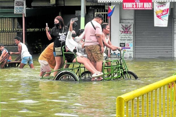 ‘FLOOD SELFIE’   Passengers of a pedicab take out their mobile phones for a “selfie” as they pass through a flooded street at the city center of Dagupan on July 30. For more than a week now, a large part of the city has been flooded due to the recent heavy rains, high tide and overflowing rivers. —WILLIE LOMIBAO